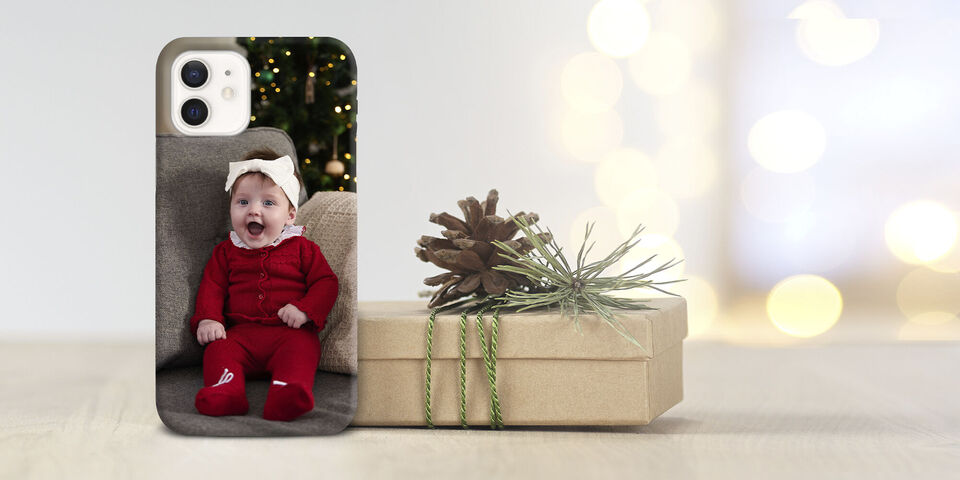 A cute child in a red Christmas suit sitting on a gray sofa with a gift and Christmas decorations behind.