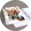 An open CEWE photo book on a table shows a charming picture of a child. A girl climbs a tree and smiles happily.